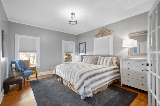 bedroom with baseboards, wood finished floors, a notable chandelier, and crown molding