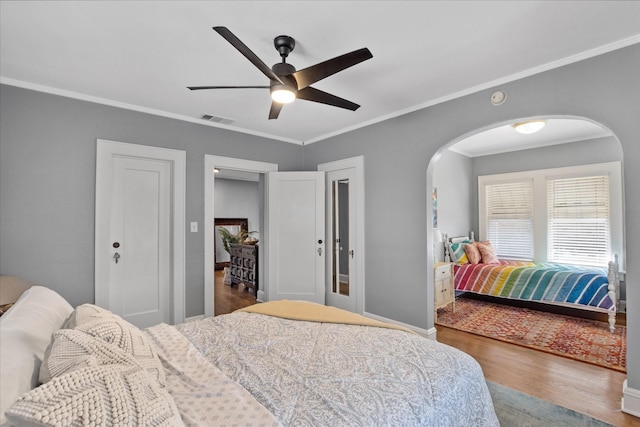 bedroom featuring wood finished floors, visible vents, crown molding, and arched walkways