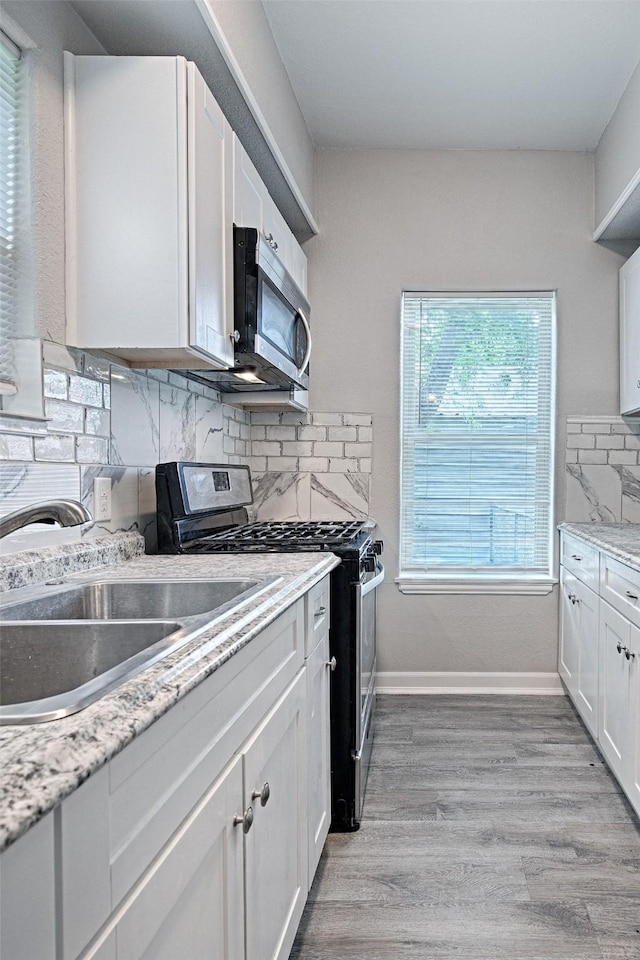 kitchen featuring light wood-style flooring, white cabinets, a sink, appliances with stainless steel finishes, and backsplash