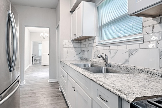 kitchen with an inviting chandelier, a sink, decorative backsplash, white cabinets, and freestanding refrigerator