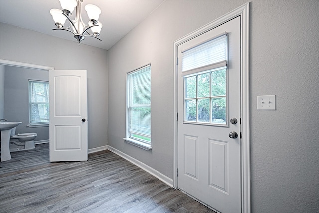 doorway with a notable chandelier, baseboards, wood finished floors, and a healthy amount of sunlight
