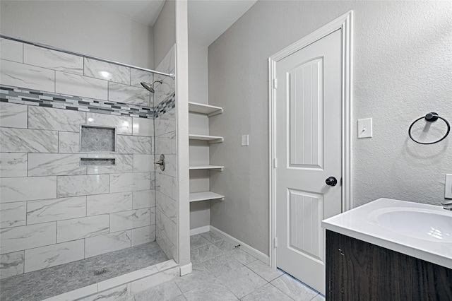 full bath with a tile shower, vanity, marble finish floor, and baseboards
