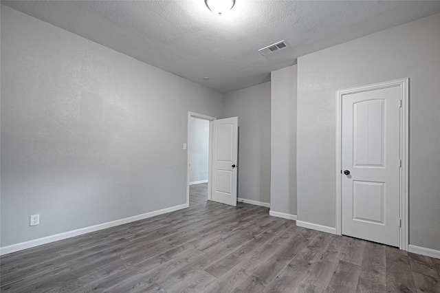 spare room featuring a textured ceiling, visible vents, wood finished floors, and baseboards