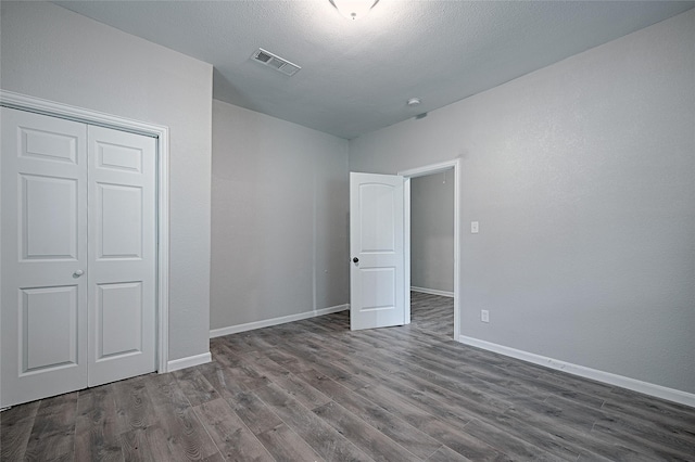unfurnished bedroom with visible vents, a closet, dark wood-style floors, and baseboards