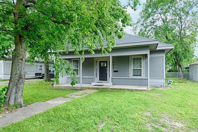 view of front of home featuring covered porch, brick siding, fence, a shingled roof, and a front lawn