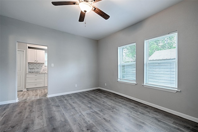 empty room with wood finished floors, a ceiling fan, and baseboards