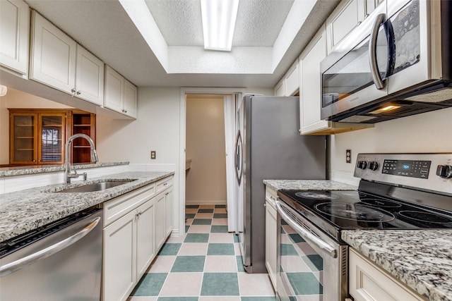 kitchen with light stone countertops, light floors, white cabinetry, a sink, and stainless steel appliances
