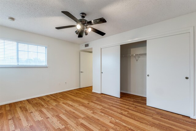 unfurnished bedroom featuring light wood-style floors, a textured ceiling, baseboards, visible vents, and a closet