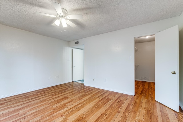 unfurnished bedroom with light wood-type flooring, a textured ceiling, a walk in closet, and visible vents