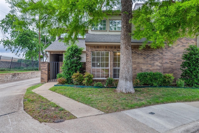 view of front of property with brick siding, fence, a shingled roof, and a front yard