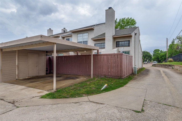 exterior space with fence, a carport, a chimney, and stucco siding