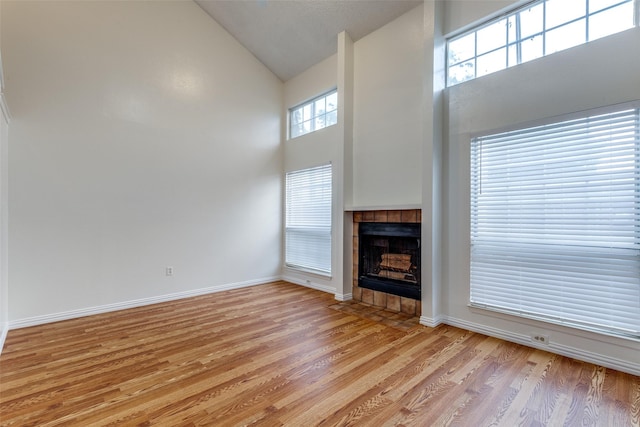 unfurnished living room featuring light wood-type flooring, baseboards, a tiled fireplace, and high vaulted ceiling