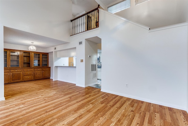 unfurnished living room featuring baseboards, visible vents, light wood-style flooring, and a towering ceiling