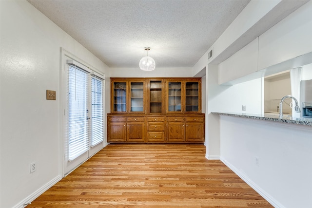 unfurnished dining area with visible vents, a textured ceiling, a chandelier, a sink, and light wood finished floors