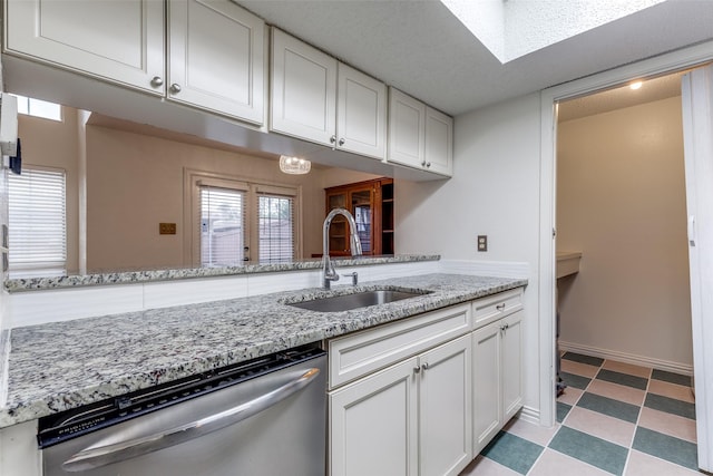 kitchen with stainless steel dishwasher, light floors, white cabinets, light stone counters, and a sink