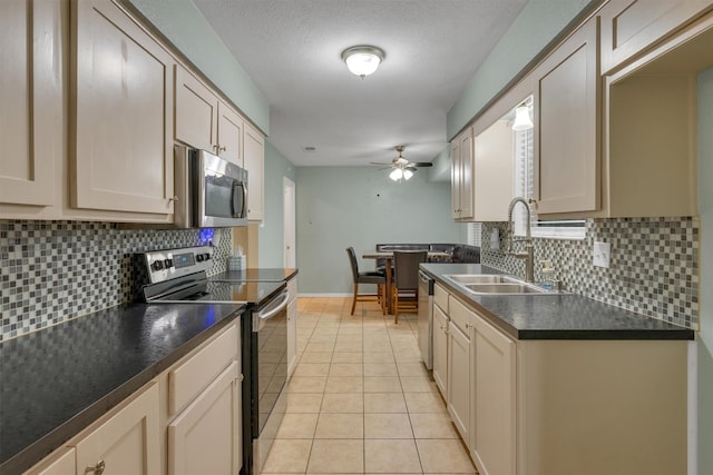 kitchen with dark countertops, a sink, stainless steel appliances, a ceiling fan, and decorative backsplash
