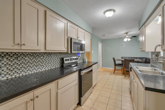 kitchen with dark countertops, ceiling fan, appliances with stainless steel finishes, a sink, and decorative backsplash