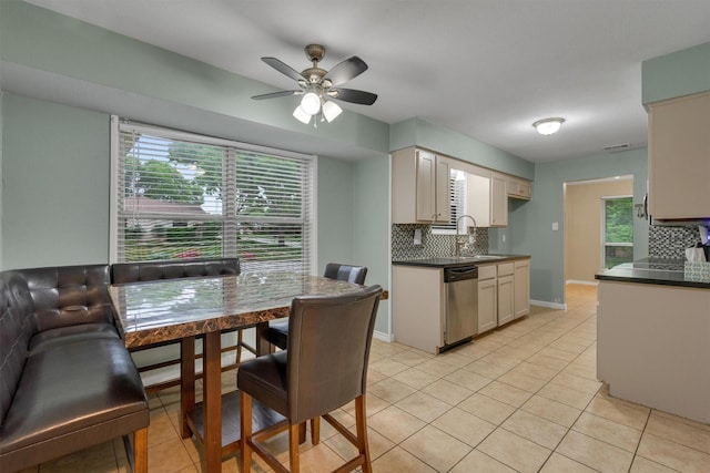 kitchen featuring stainless steel dishwasher, light tile patterned floors, backsplash, and dark countertops