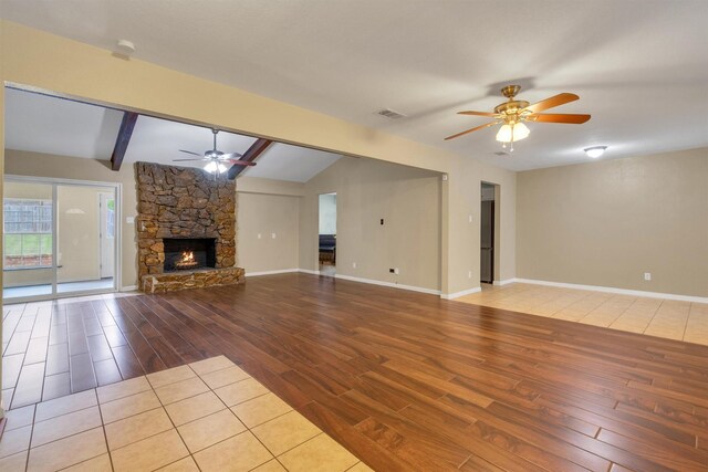 unfurnished living room with ceiling fan, a stone fireplace, visible vents, wood finished floors, and lofted ceiling with beams