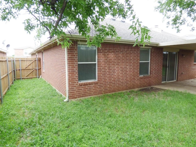 view of property exterior featuring a patio area, brick siding, a yard, roof with shingles, and fence