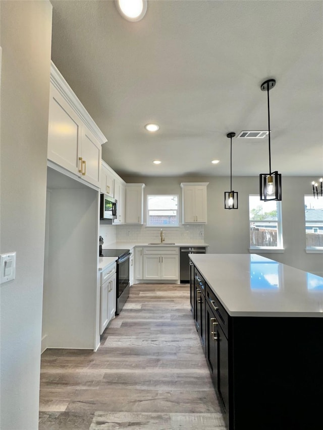 kitchen with white cabinets, light wood-type flooring, appliances with stainless steel finishes, and light countertops
