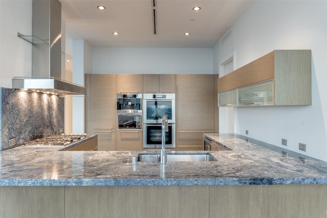 kitchen with a sink, stainless steel appliances, stone countertops, recessed lighting, and wall chimney exhaust hood