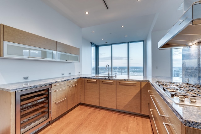 kitchen with stainless steel gas cooktop, a sink, under cabinet range hood, wine cooler, and light wood-style flooring