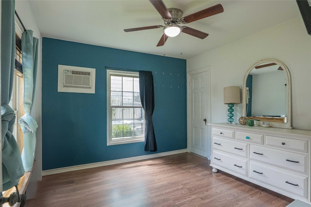 unfurnished bedroom with baseboards, a wall mounted air conditioner, a ceiling fan, and light wood finished floors