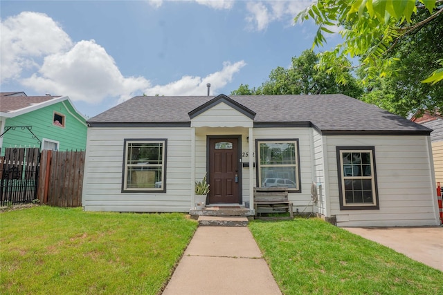 bungalow-style home with a front lawn, roof with shingles, and fence