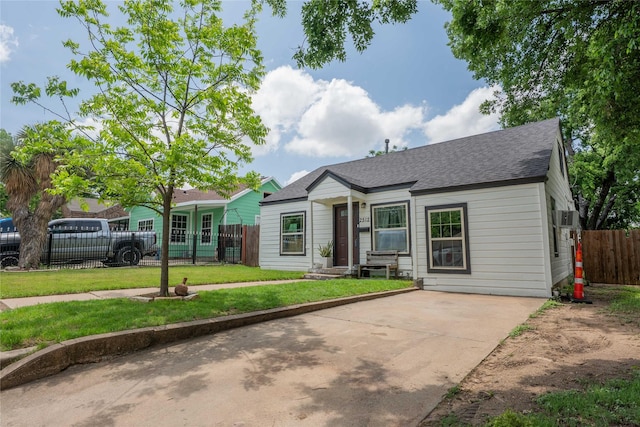 view of front of home with fence private yard, roof with shingles, a wall mounted air conditioner, a front yard, and concrete driveway