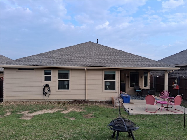 rear view of house with a patio, an outdoor fire pit, a yard, and roof with shingles