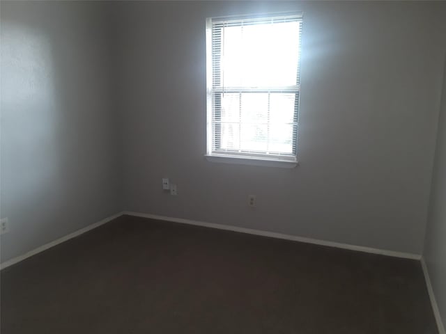 unfurnished room with dark carpet and baseboards