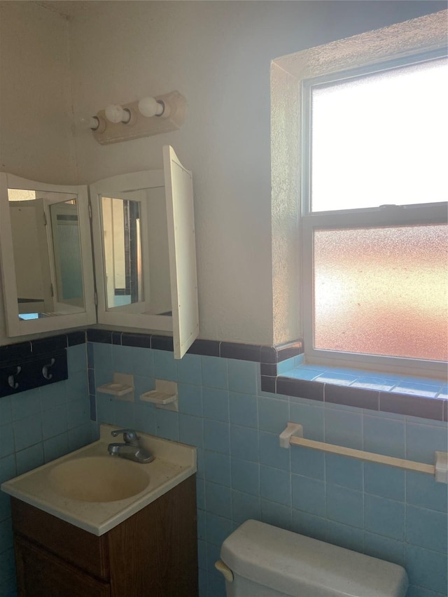 bathroom featuring toilet, tile walls, vanity, and a healthy amount of sunlight