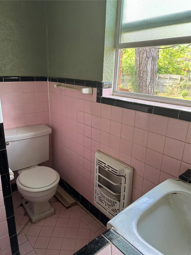 bathroom with toilet, heating unit, tile walls, and a wealth of natural light