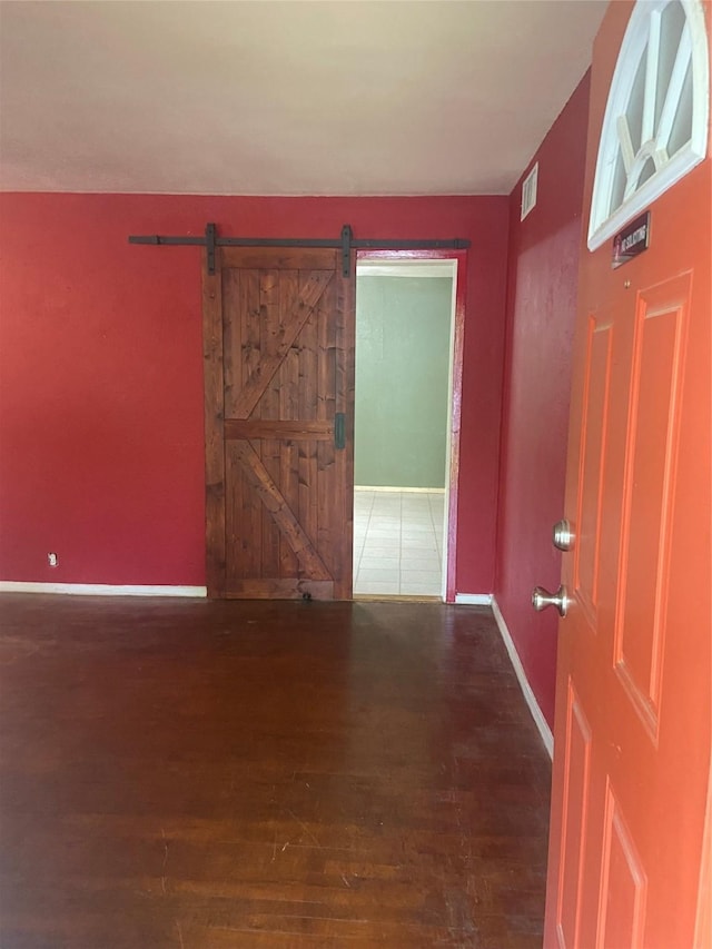 spare room featuring wood finished floors, visible vents, baseboards, and a barn door