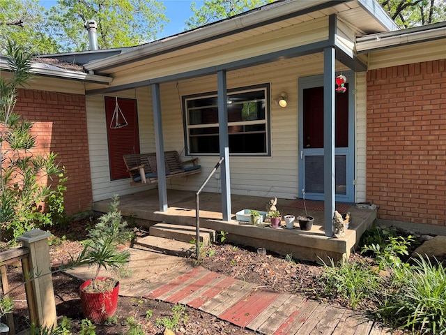view of exterior entry with brick siding and a porch