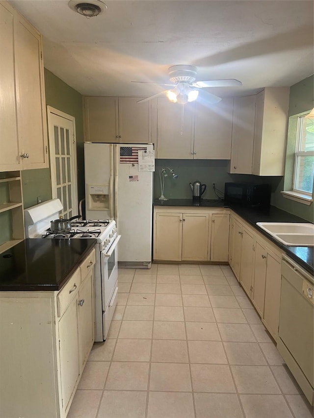 kitchen featuring a sink, light tile patterned floors, a ceiling fan, white appliances, and dark countertops