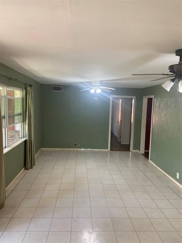 empty room with light tile patterned floors, visible vents, a ceiling fan, and baseboards
