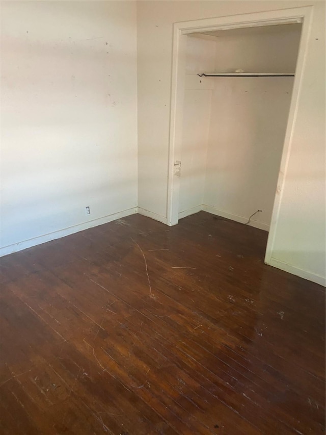 unfurnished bedroom featuring baseboards, a closet, and dark wood-type flooring