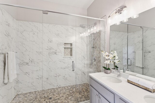 full bathroom with a sink, a marble finish shower, and double vanity