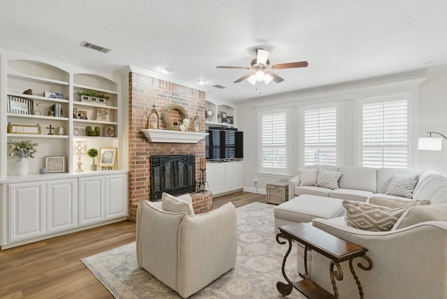 living room with ornamental molding, a fireplace, light wood finished floors, visible vents, and a ceiling fan