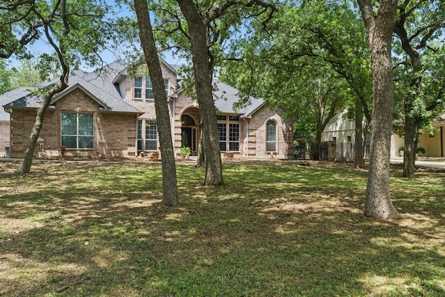 traditional-style house with a front lawn, a shingled roof, and brick siding