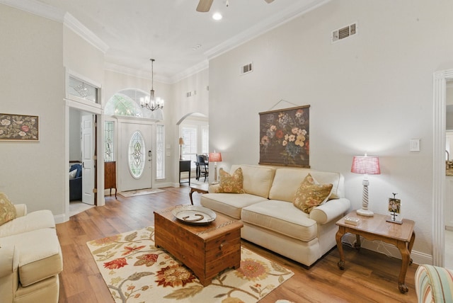 living area with light wood finished floors, visible vents, a towering ceiling, arched walkways, and ceiling fan with notable chandelier