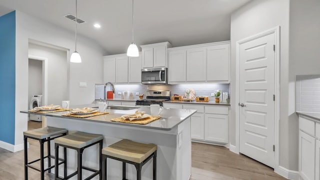 kitchen featuring tasteful backsplash, a sink, appliances with stainless steel finishes, a kitchen bar, and washer / dryer