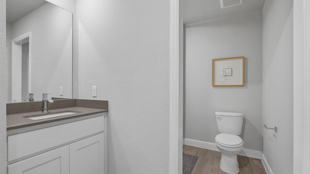 bathroom featuring vanity, toilet, visible vents, baseboards, and wood finished floors
