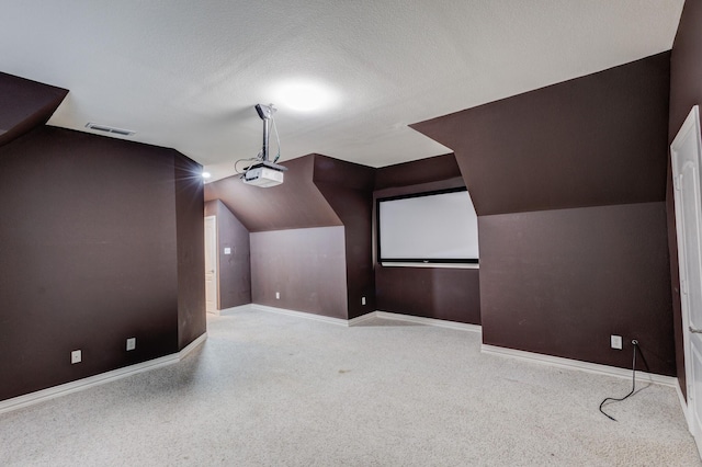 home theater room featuring a textured ceiling, visible vents, vaulted ceiling, and baseboards