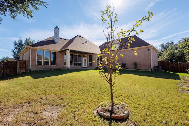 rear view of property with a lawn, a chimney, a fenced backyard, and brick siding