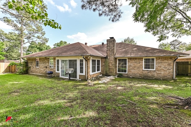 back of house with a chimney, a yard, brick siding, fence, and a shingled roof