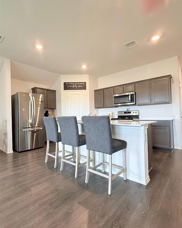 kitchen featuring appliances with stainless steel finishes, a kitchen breakfast bar, dark wood-type flooring, and visible vents
