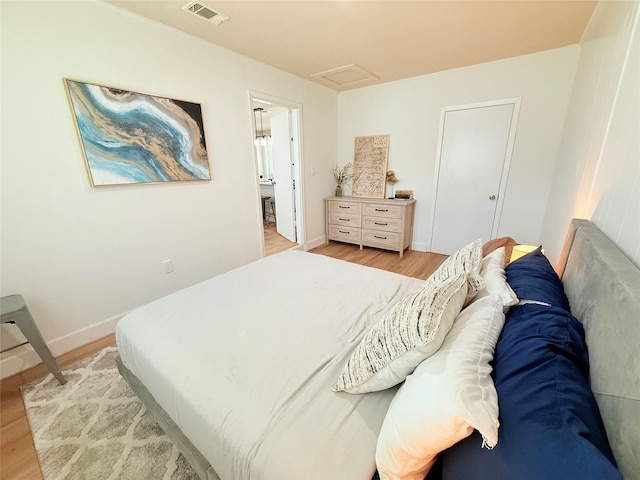bedroom with attic access, visible vents, light wood-type flooring, and baseboards